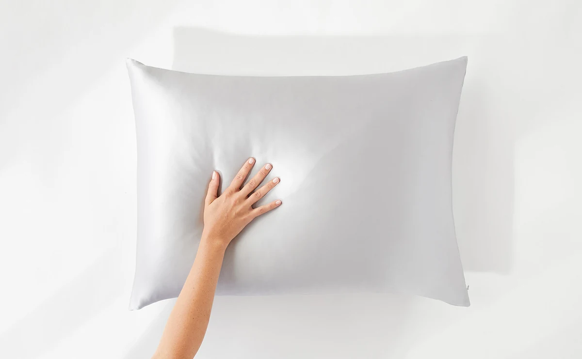 A hand resting on a pale gray Promeed silk pillowcase