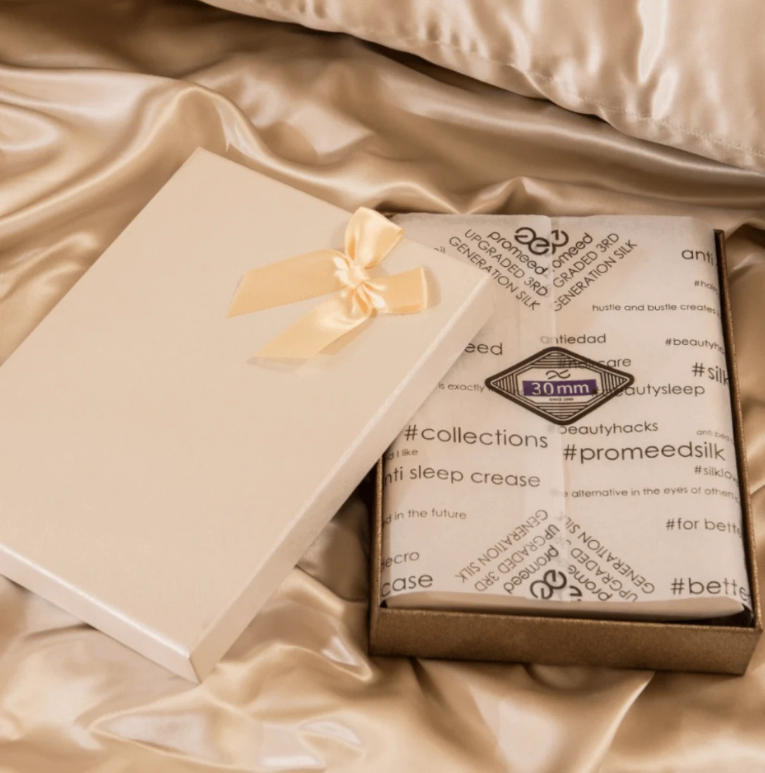 Promeed silk pillowcase and gift packaging on champagne-colored fabric